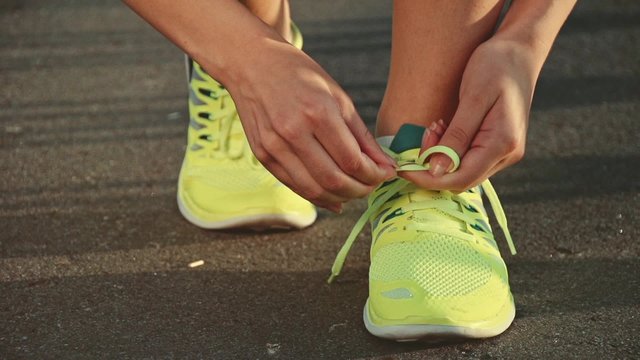 Slow motion: running shoes. Barefoot running shoes closeup. Female athlete tying laces for jogging on road in minimalistic barefoot running shoes. Runner getting ready for training. Sport lifestyle.