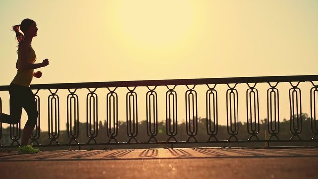 Slow motion: running woman. Runner is jogging in sunny bright light. Female fitness model training outside in the city on a quay. Sport lifestyle. Filmed at 240 fps.