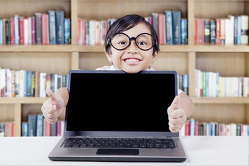 Child shows hand gesture with laptop in library