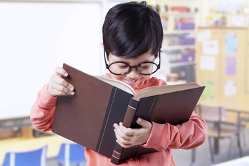 Cute student standing in class while reading book