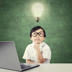 Genius child with laptop thinks idea under lamp