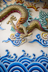 Golden scaled dragon flying above stylized blue waves in Asian scene decorating Buddhist temple in Bangkok Thailand