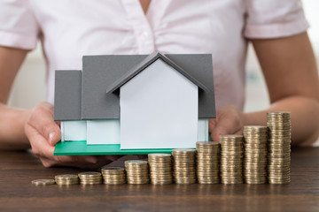 Businesswoman With House Model And Stack Of Coins