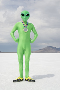 Green alien athlete wearing gold medal standing on stark white planet background