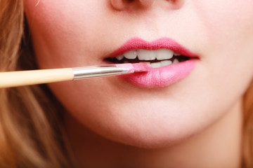 Naklejka premium Part of face. Woman applying pink lipstick with brush