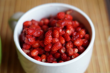 Red fresh wild strawberry in a big white mug stand on a table