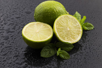 Green limes with mint and water drops on black background