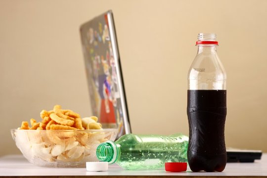 Bottles of softdrinks or soda, chips and a laptop computer in the background