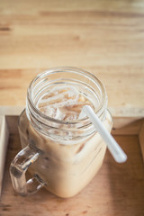 Iced coffee with milk is in Mason jar , on the table.
