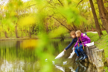Naklejka na ściany i meble Boy and girl near the pond play with paper boats