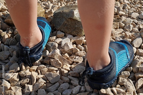 5 Years Old Boy Feet With Aquatic Blue Shoes On Rocky Beach Stock 5 Years Old Boy Feet With Aquatic Blue Shoes On Rocky Beach