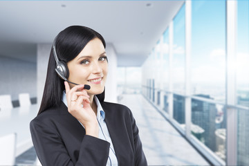 Portrait of smiling cheerful support phone operator in headset. Modern panoramic office.