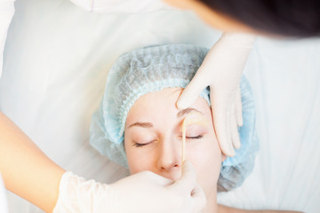 Professional woman at spa beauty salon doing epilation or correction eyebrow using sugar  - sugaring. You can see her smooth eyebrow after hair removal