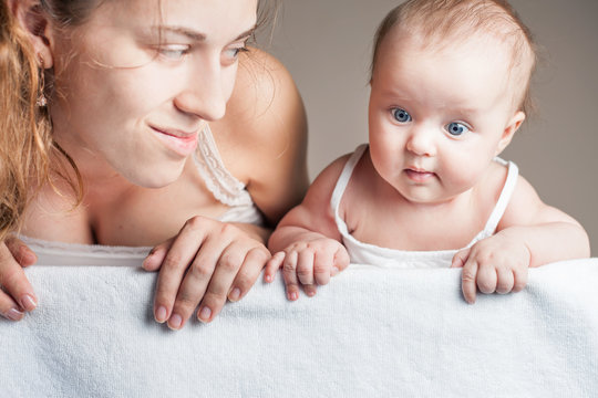 Mother and baby lying on a white blanket. Advertising banner sign - Mom is pointing down and baby looking down on empty blank billboard or sign board. There is a copy space for text and design