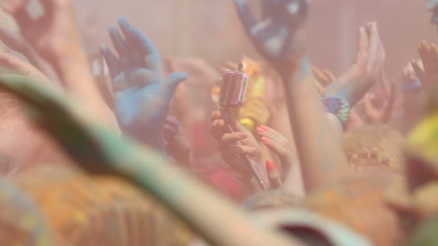 Crowd throwing hands up in air at Holi colors festival.
