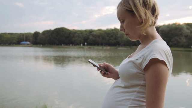Pregnant woman using mobile phone in park