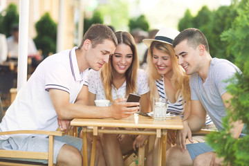 Group of young friends sitting in a cafe looking at mobile phone