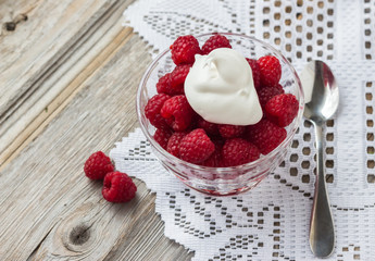 image of a glass bowl of raspberries topped with whipped cream on an old wood surface covered partially with lace with empty text space.