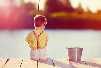 Foto op Plexiglas cute little boy fishing on pond at sunset © Olesia Bilkei