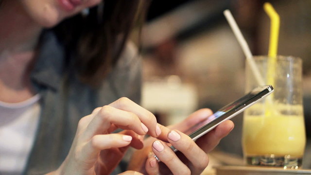 Woman hands browsing photos on smartphone and drinking cocktail sitting in cafe 

