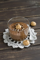chocolate mousse with nuts and biscuits in a glass beaker on a dark wooden background