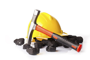 Yellow helmet with mining pickax and loose lumps of black coal on white glossy table