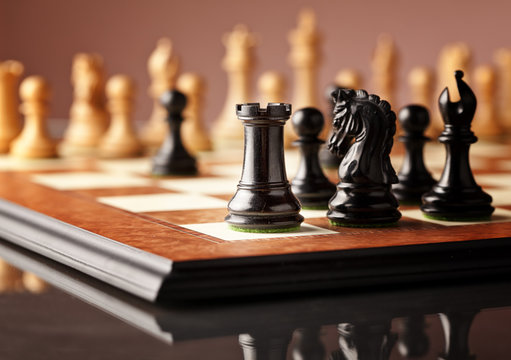 Traditional Staunton chess pieces (black rook in focus) carved in genuine ebony standing on the elm burl and bird's eye maple superior chessboard and glossy table