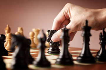 Male hand moving the black chess knight in focus in the middle of a game of chess