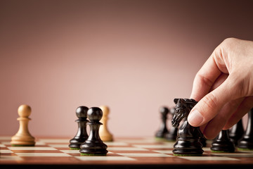 Male hand holding the black chess knight in focus at the end of a chess game