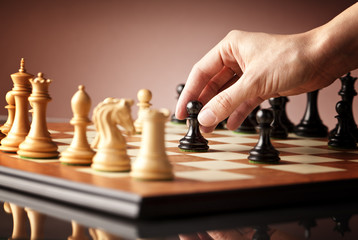 Playing chess - a hand moving black pawn on a traditional wooden chessboard
