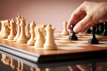 Male hand moving the black pawn in focus on the luxury elm burl and bird's eye maple superior chessboard at the beginning of chess game