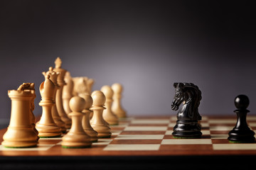 Black chess knight and pawn facing the entire army of white chess pieces on a wooden chessboard in focus