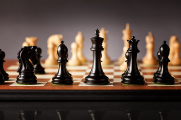 Setup of a chess game - black pieces in focus standing on a wooden chessboard