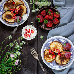Pancakes with wild berries on dark wooden table.