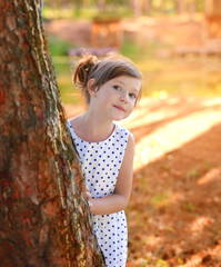 A girl looks out from behind a tree