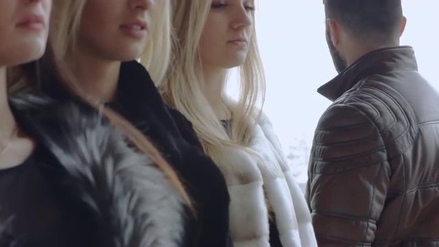A young bearded man looks at three women in expensive furs and