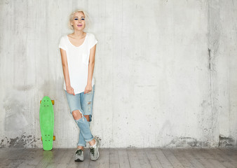 Blonde with a skate in a white T-shirt against the background of a concrete wall