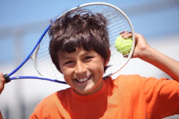 Tuinposter Young boy outside in sun with tennis racquet and ball - portrait format with copy space above © Nicholas B