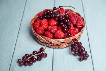 Red currant and raspberry in a basket on a white wooden background