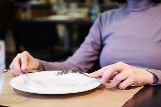 Female hands at dinner table holding fork and a knife above empty white plate