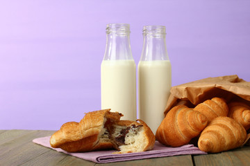 Croissants in a basket and a glass of milk on wooden background