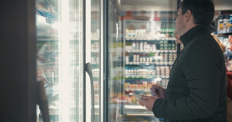 Young couple taking frozen food from fridge in the shop - Powered by Adobe
