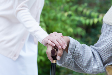 杖を握った男性患者の手に手を添える女性看護師