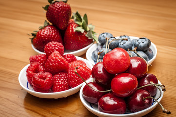 Small bowls of fruit containing cherries, strawberries, blueberries and rasberries on a wooden table