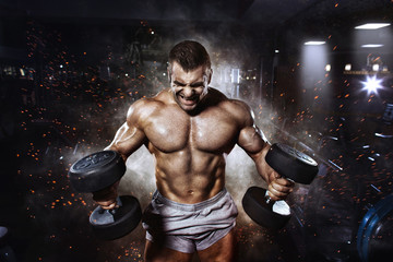 Fototapeta na wymiar Athlete muscular bodybuilder in the gym training with dumbbells