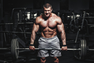 Naklejka na ściany i meble Athlete muscular bodybuilder in the gym training with barbell