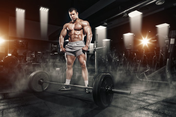Athlete muscular bodybuilder in the gym training with barbell and posing hard
