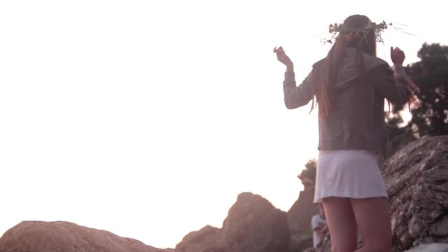 Girl in a wreath is on the rocks, affably waving his arms
