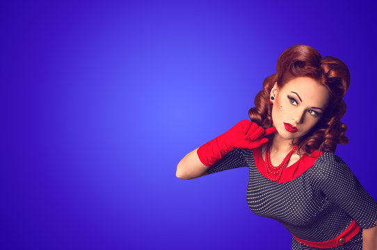 Red hair beautiful curious pin-up girl on a blue background with copy space 