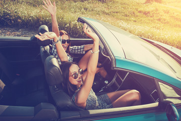 Two attractive young women in a convertible car - obrazy, fototapety, plakaty